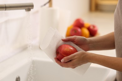 Photo of Woman wiping apple with paper towel above sink in kitchen, closeup