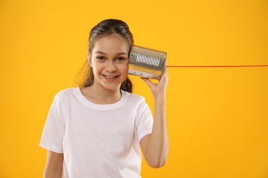 Photo of Girl using tin can telephone on yellow background