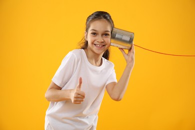 Photo of Girl using tin can telephone on yellow background