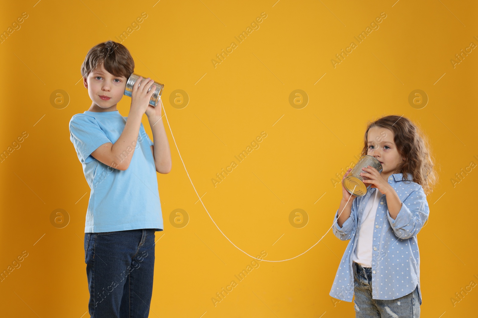 Photo of Boy and girl talking on tin can telephone against orange background