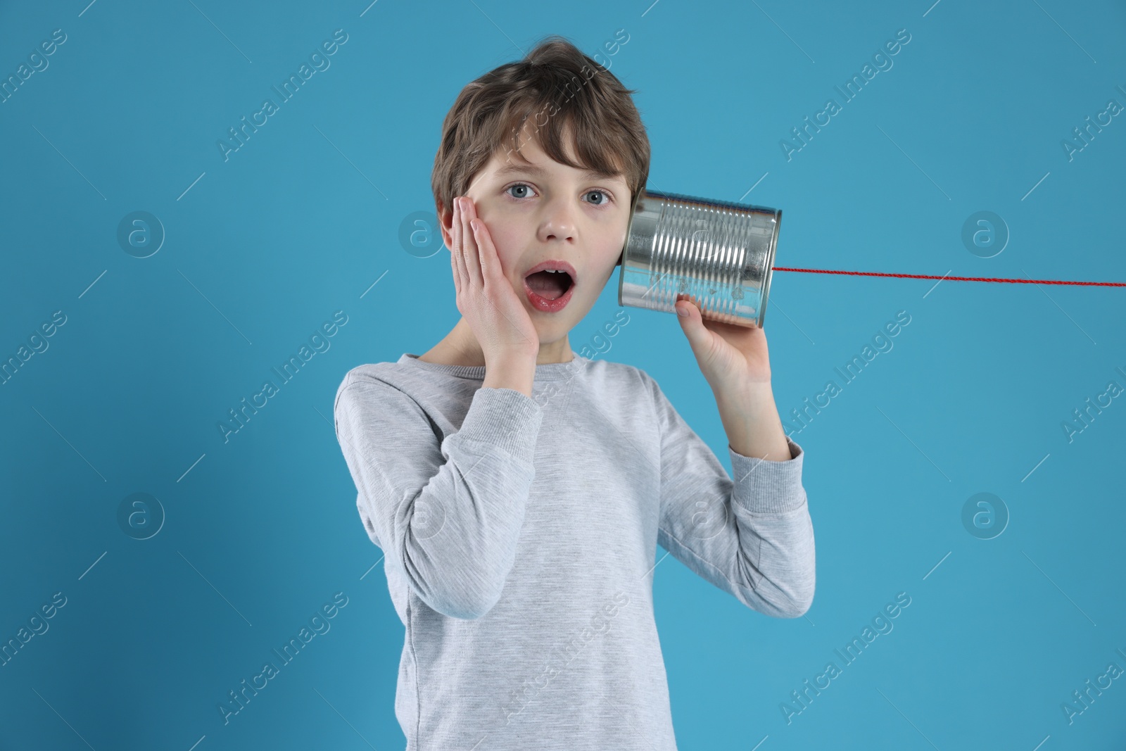 Photo of Surprised boy using tin can telephone on blue background