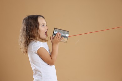 Photo of Girl using tin can telephone on beige background