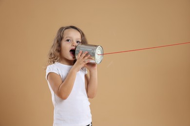 Photo of Girl using tin can telephone on beige background