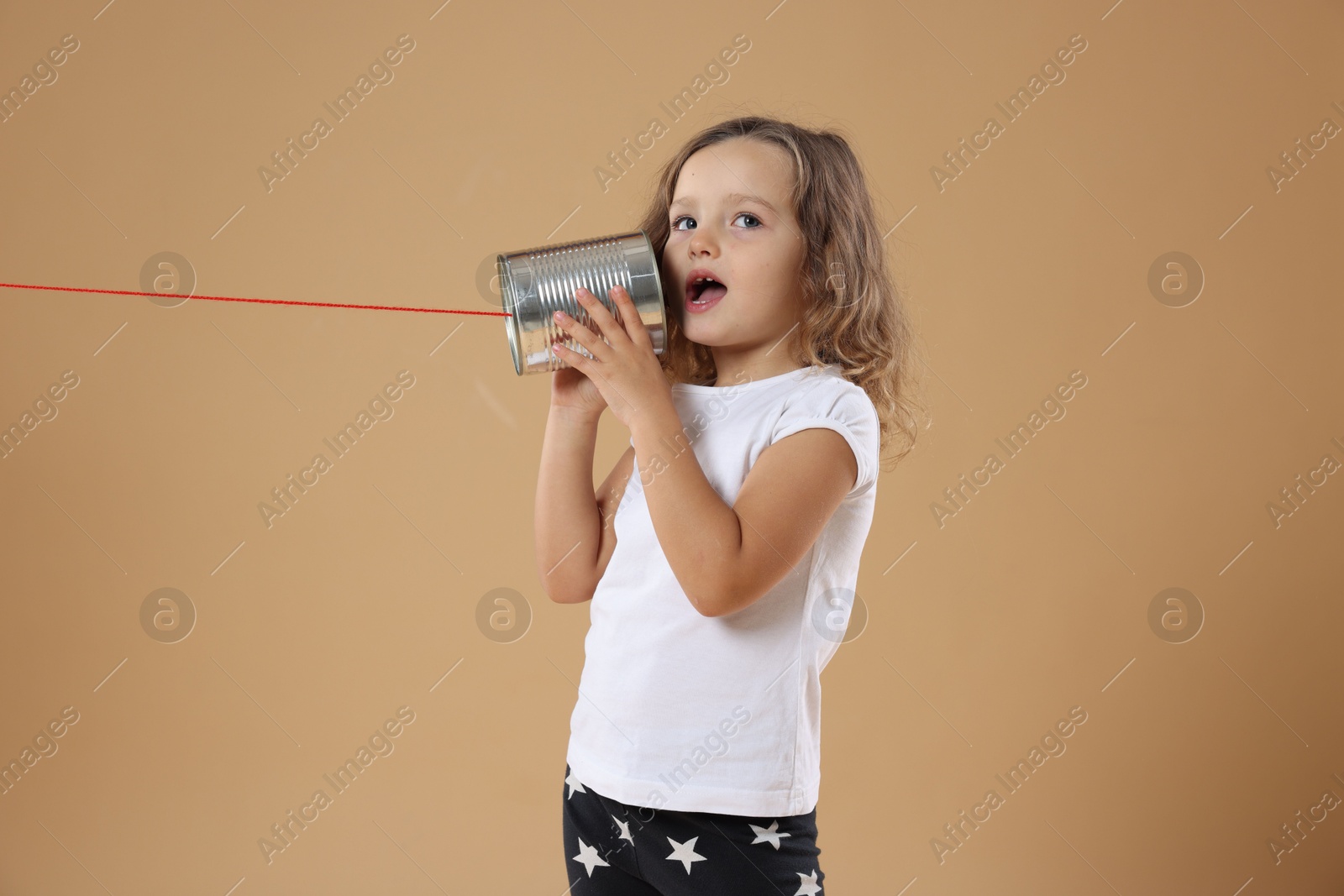 Photo of Girl using tin can telephone on beige background