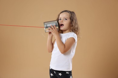 Photo of Girl using tin can telephone on beige background