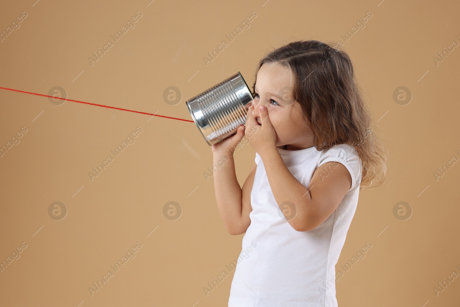 Photo of Excited girl using tin can telephone on beige background