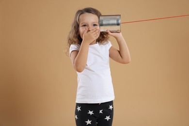 Photo of Excited girl using tin can telephone on beige background