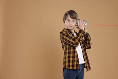 Photo of Boy using tin can telephone on beige background. Space for text