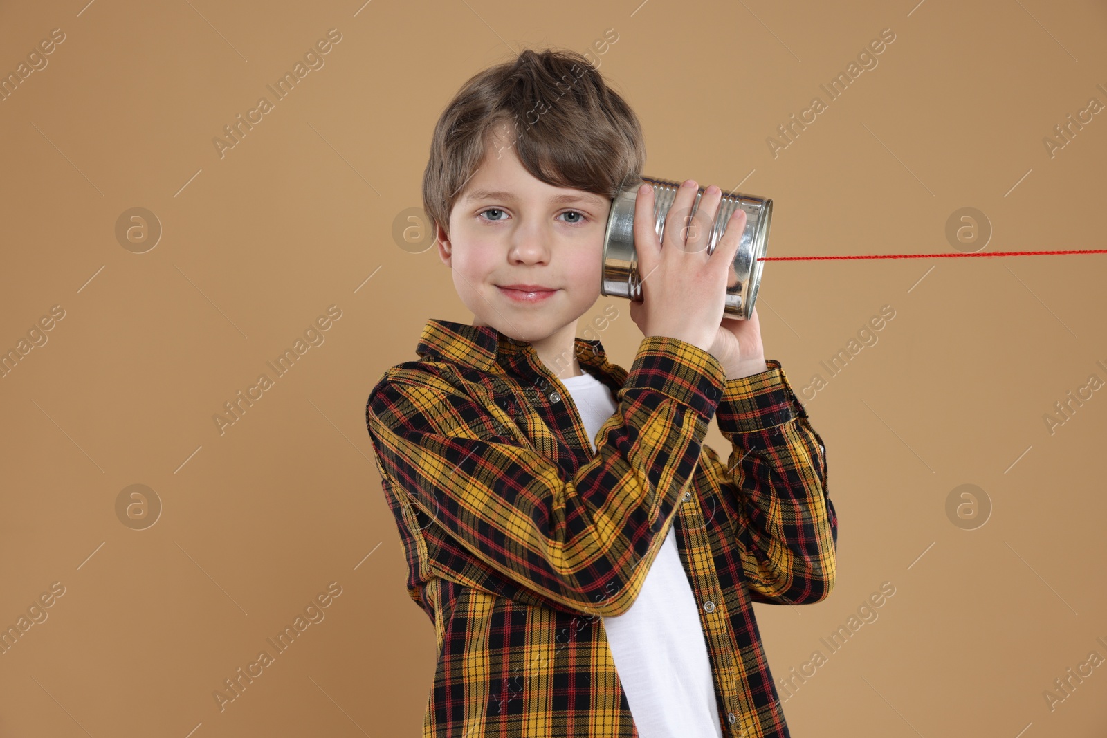 Photo of Boy using tin can telephone on beige background