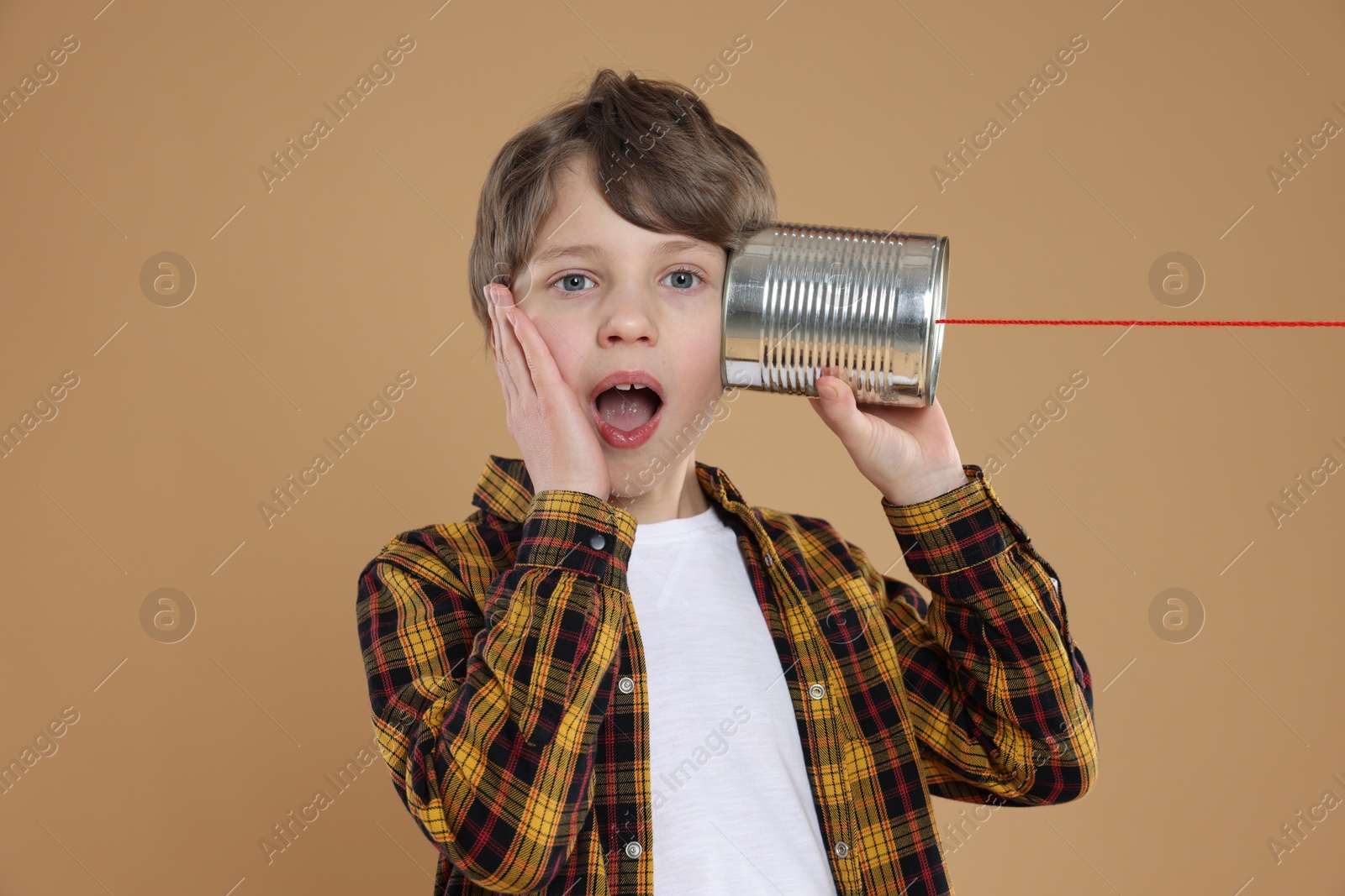 Photo of Surprised boy using tin can telephone on beige background