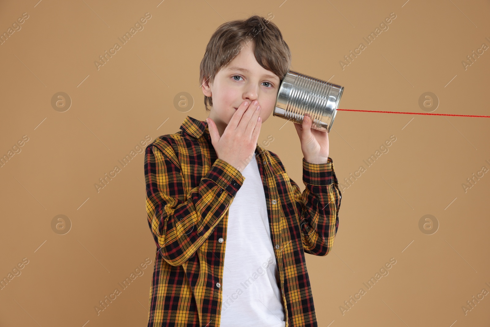 Photo of Surprised boy using tin can telephone on beige background