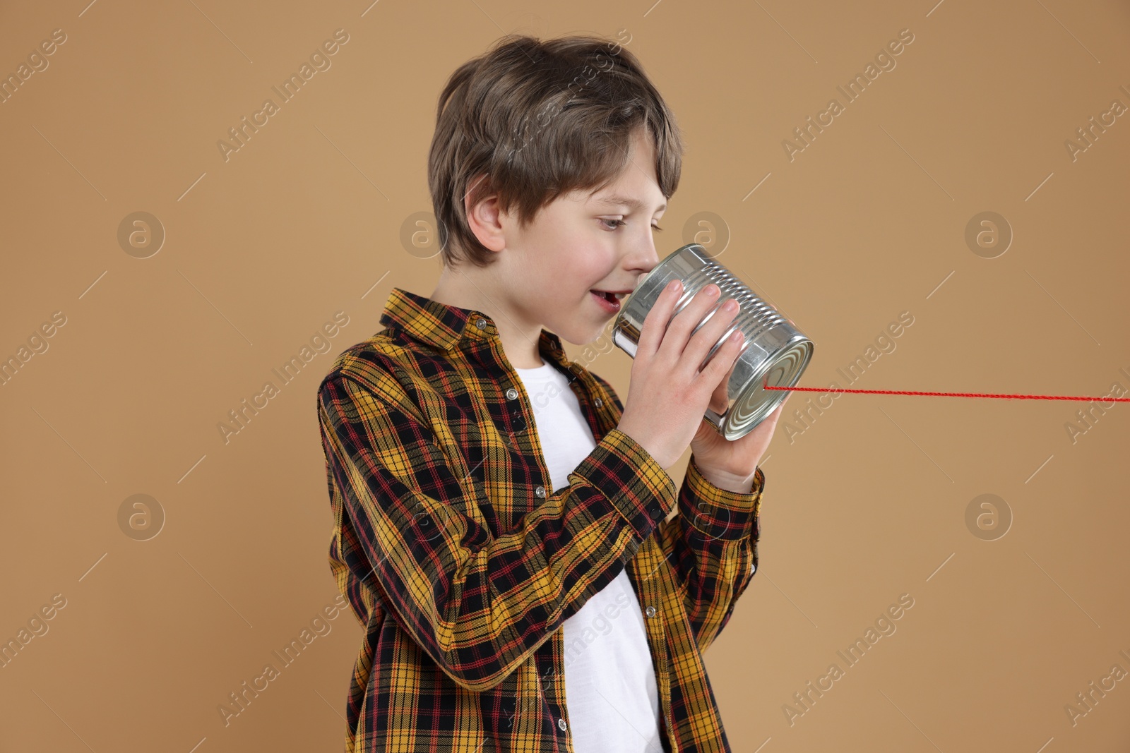 Photo of Boy using tin can telephone on beige background