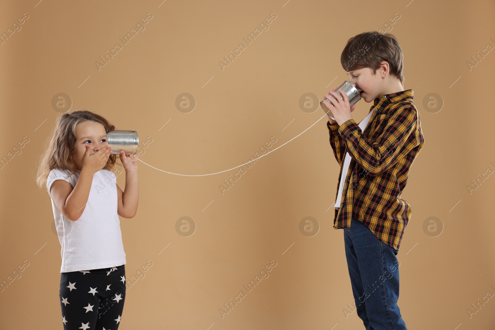 Photo of Boy and girl talking on tin can telephone against beige background