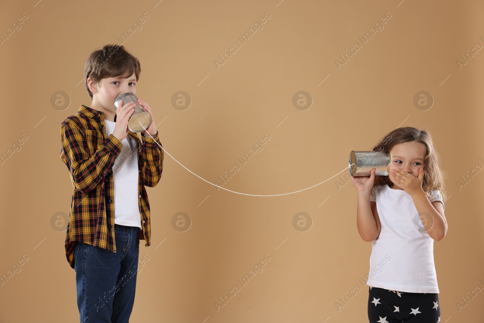 Photo of Boy and girl talking on tin can telephone against beige background