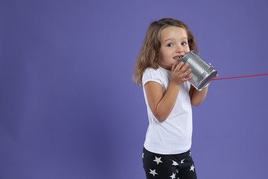 Photo of Girl using tin can telephone on violet background. Space for text