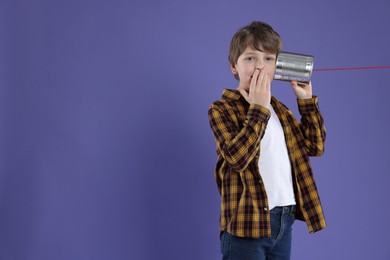 Photo of Boy using tin can telephone on violet background. Space for text