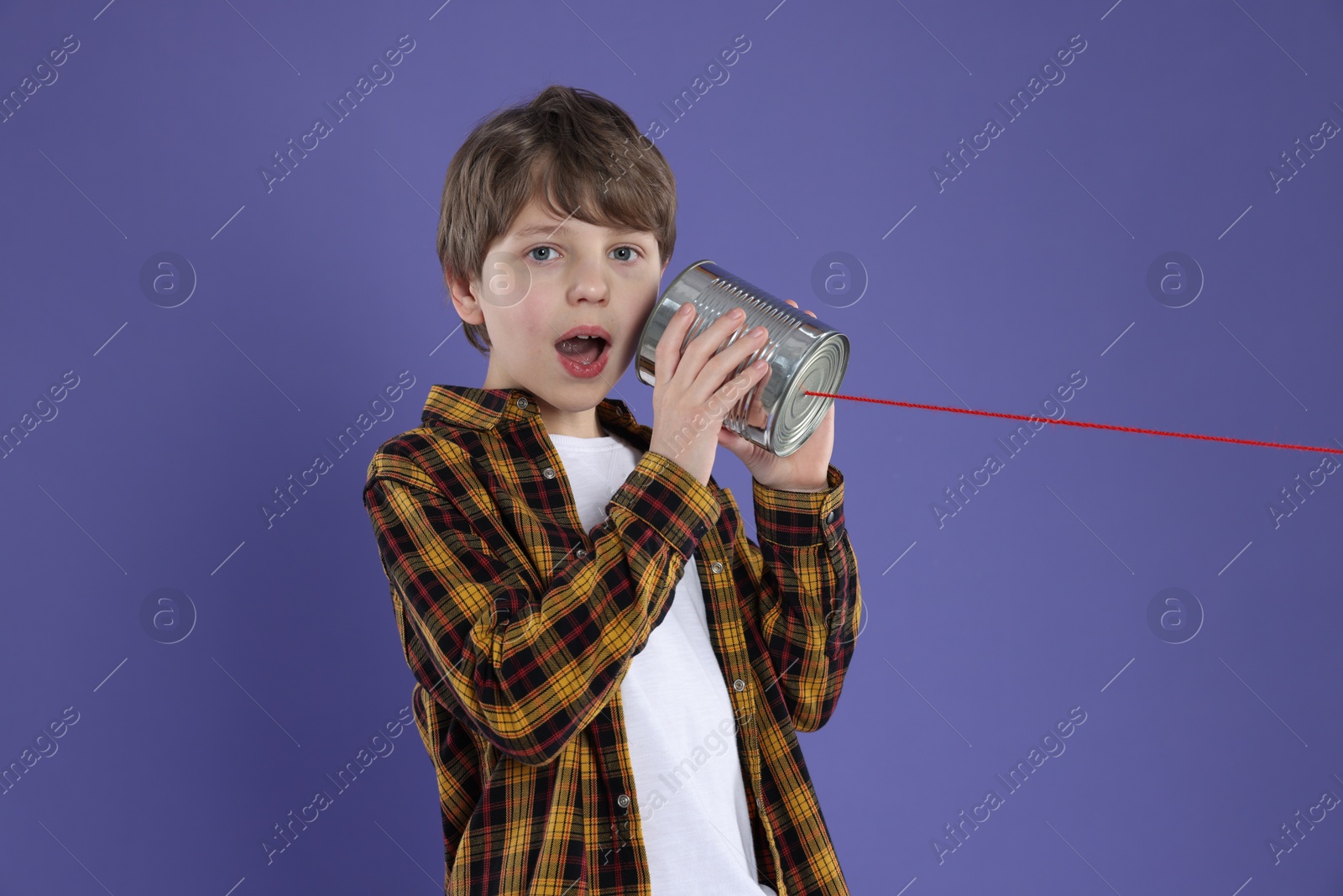 Photo of Boy using tin can telephone on violet background