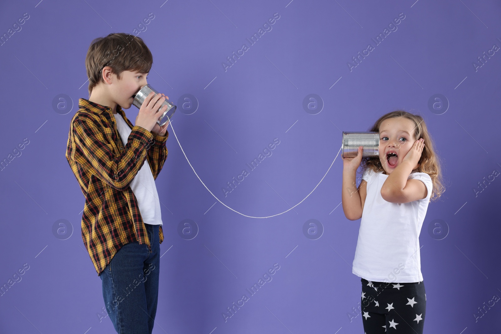 Photo of Boy and girl talking on tin can telephone against violet background