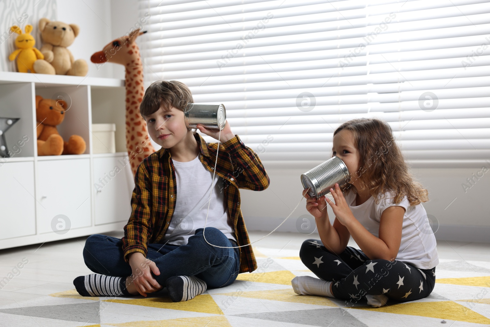 Photo of Boy and girl talking on tin can telephone indoors