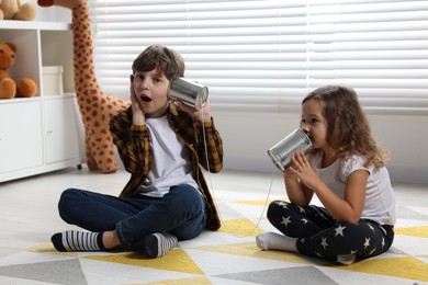 Photo of Boy and girl talking on tin can telephone indoors