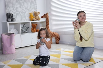 Photo of Woman and girl talking on tin can telephone indoors