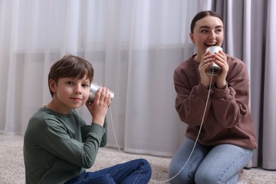 Photo of Woman and boy talking on tin can telephone indoors