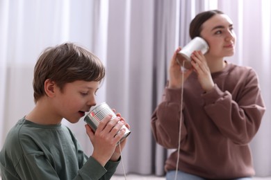 Photo of Woman and boy talking on tin can telephone indoors