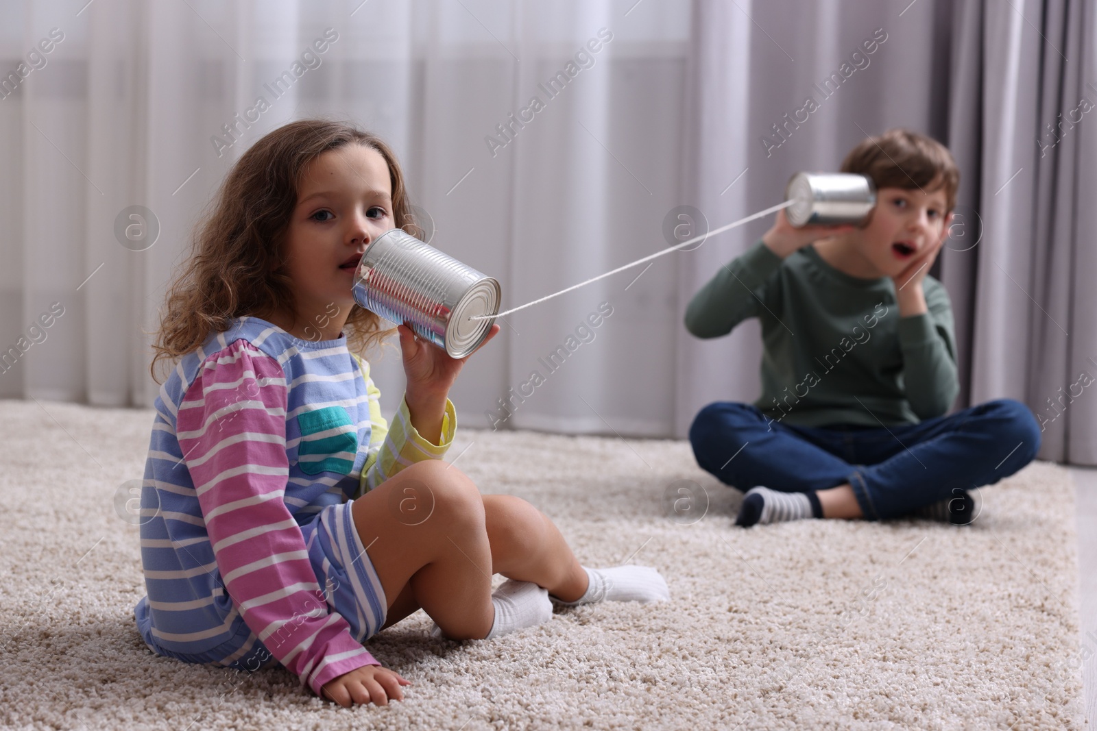 Photo of Boy and girl talking on tin can telephone indoors, selective focus