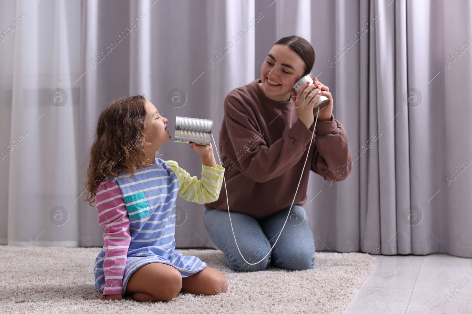 Photo of Woman and girl talking on tin can telephone indoors