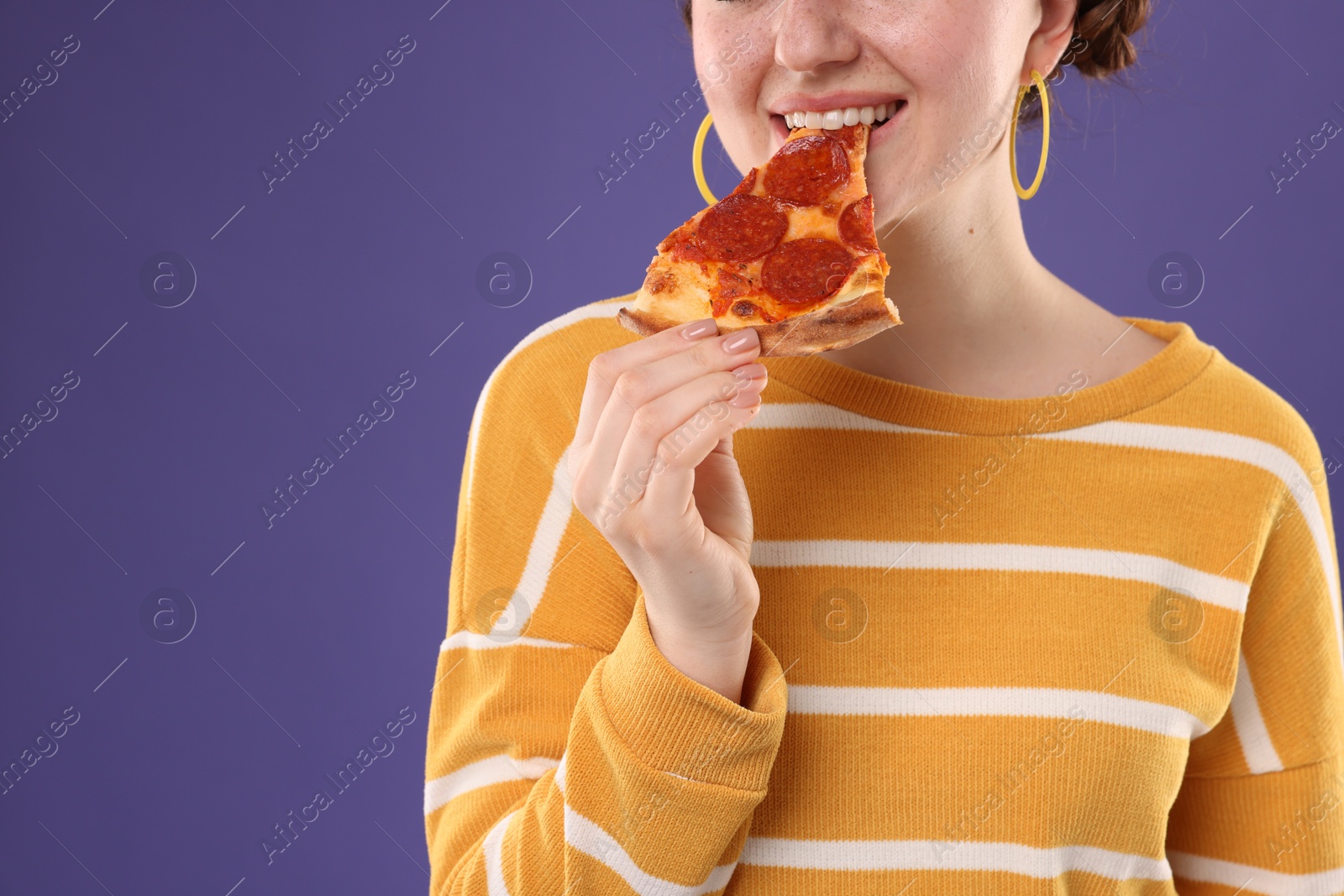 Photo of Woman eating pizza on violet background, closeup