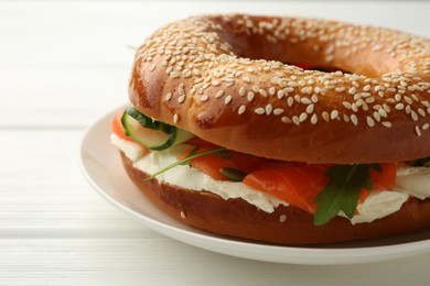 Photo of Delicious bagel with salmon, cream cheese and cucumber on white wooden table, closeup