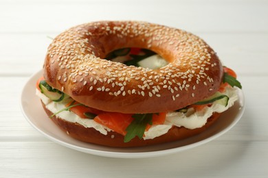 Photo of Delicious bagel with salmon, cream cheese and arugula on white wooden table, closeup