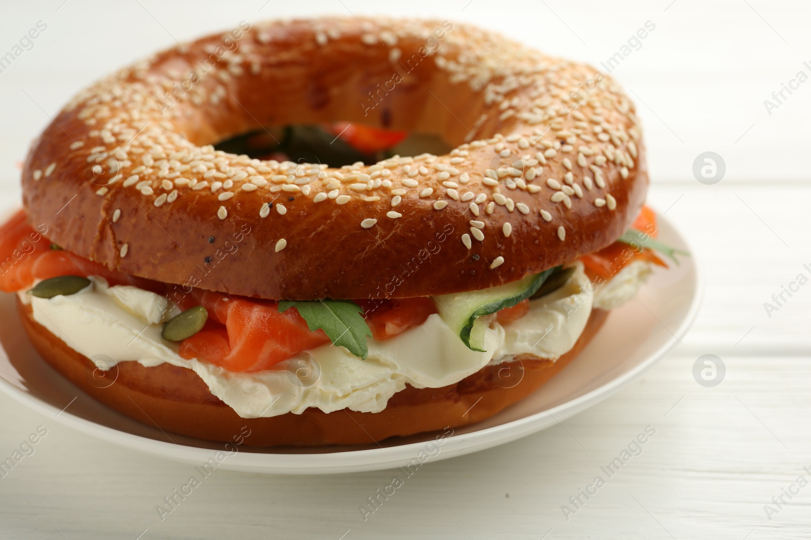 Photo of Delicious bagel with salmon and cream cheese on white wooden table, closeup