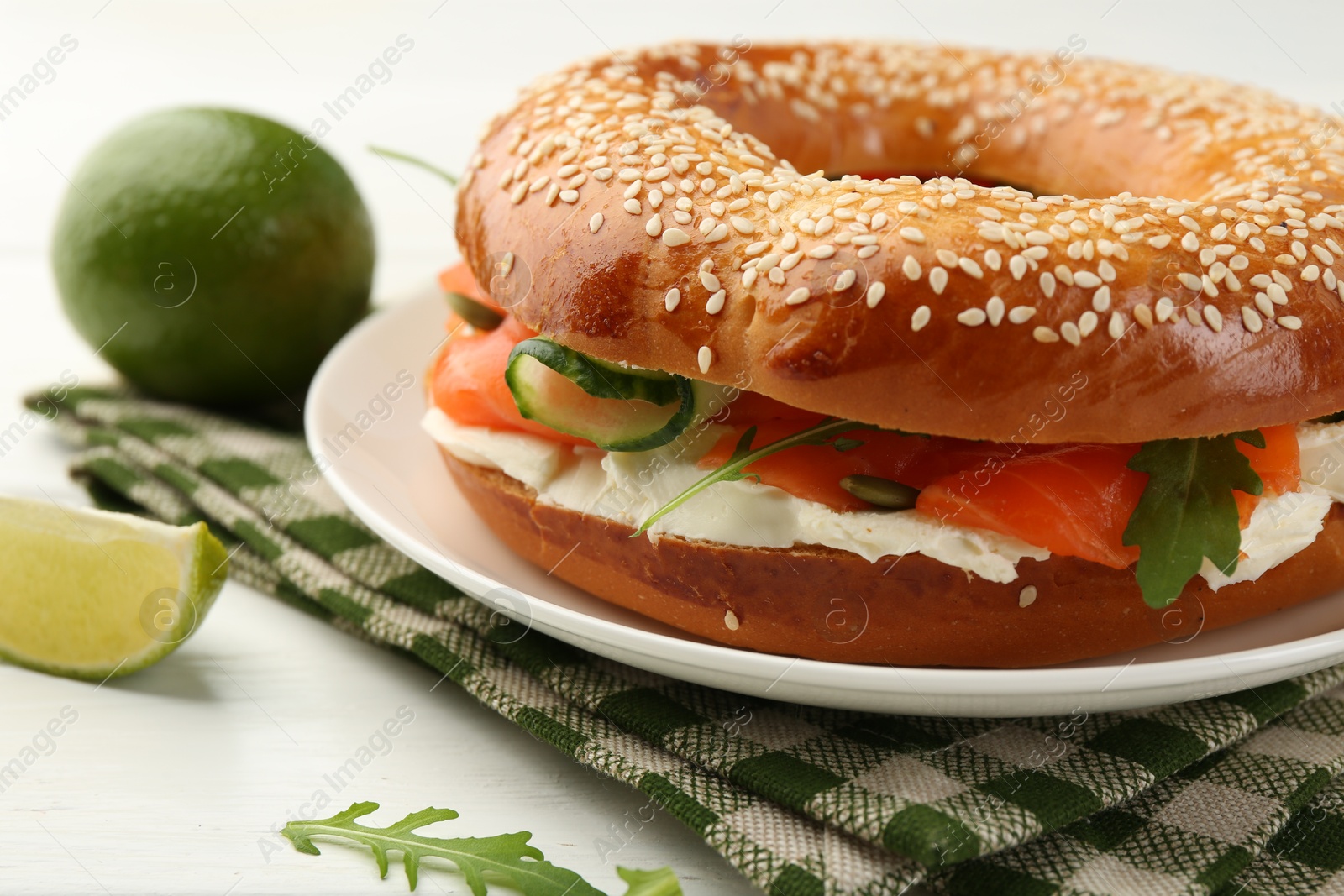 Photo of Delicious bagel with salmon, arugula and cream cheese on white wooden table, closeup