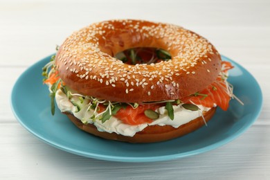 Photo of Delicious bagel with salmon, microgreens, arugula and cream cheese on white wooden table, closeup