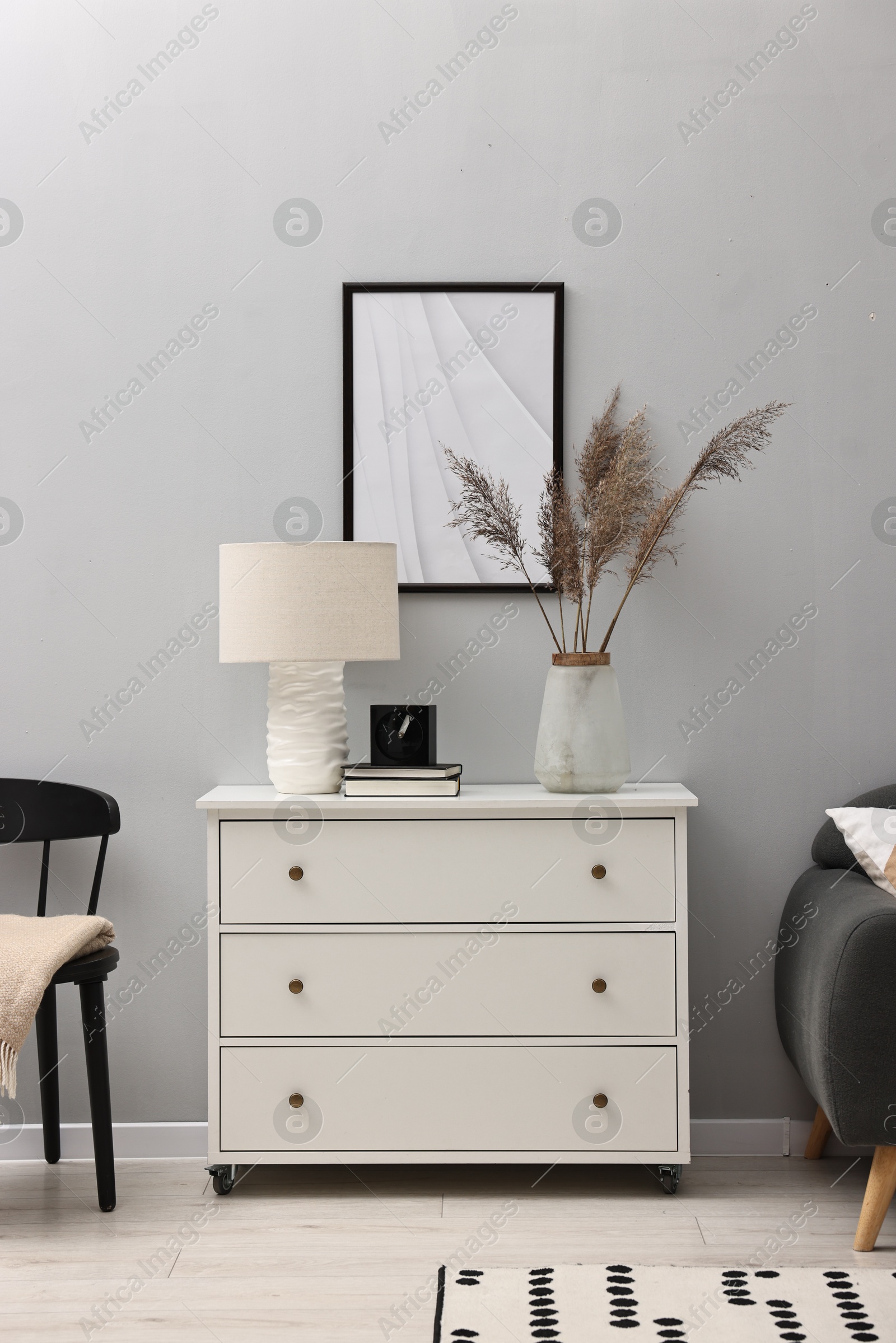 Photo of Dresser with lamp and decor near light grey wall in room. Interior design