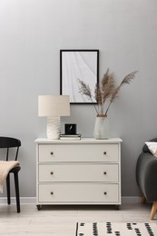 Photo of Dresser with lamp and decor near light grey wall in room. Interior design