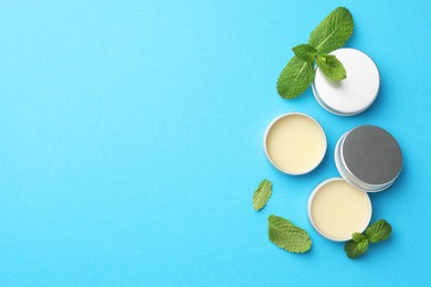 Photo of Natural lip balms and mint leaves on light blue background, flat lay. Space for text