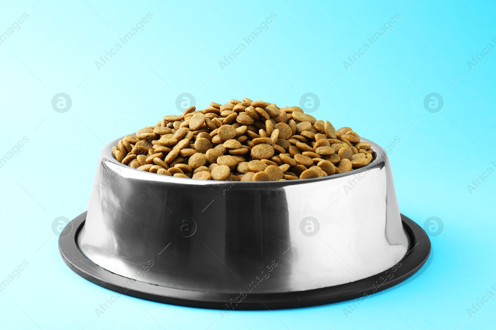 Photo of Dry pet food in feeding bowl on light blue background