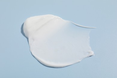 Photo of Sample of cream on light blue background, closeup. Cosmetic product