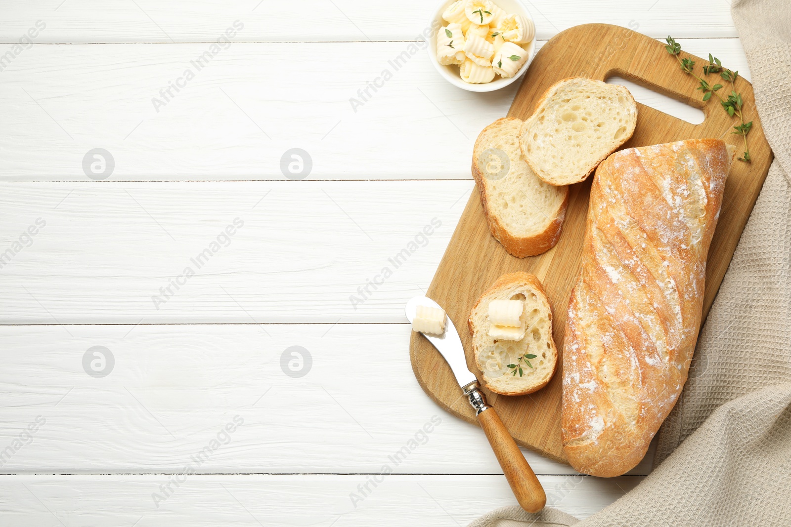 Photo of Cut baguette with butter and herbs on white wooden table, flat lay. Space for text