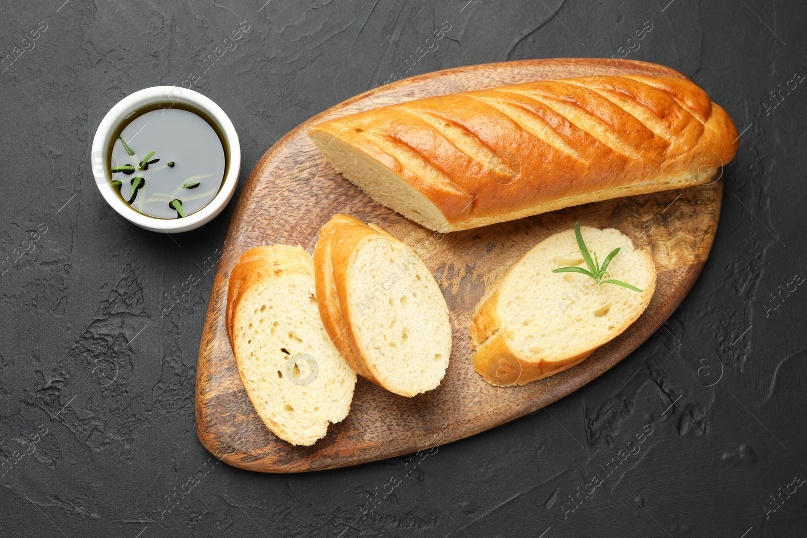 Photo of Cut fresh baguette with balsamic and rosemary on black table, top view