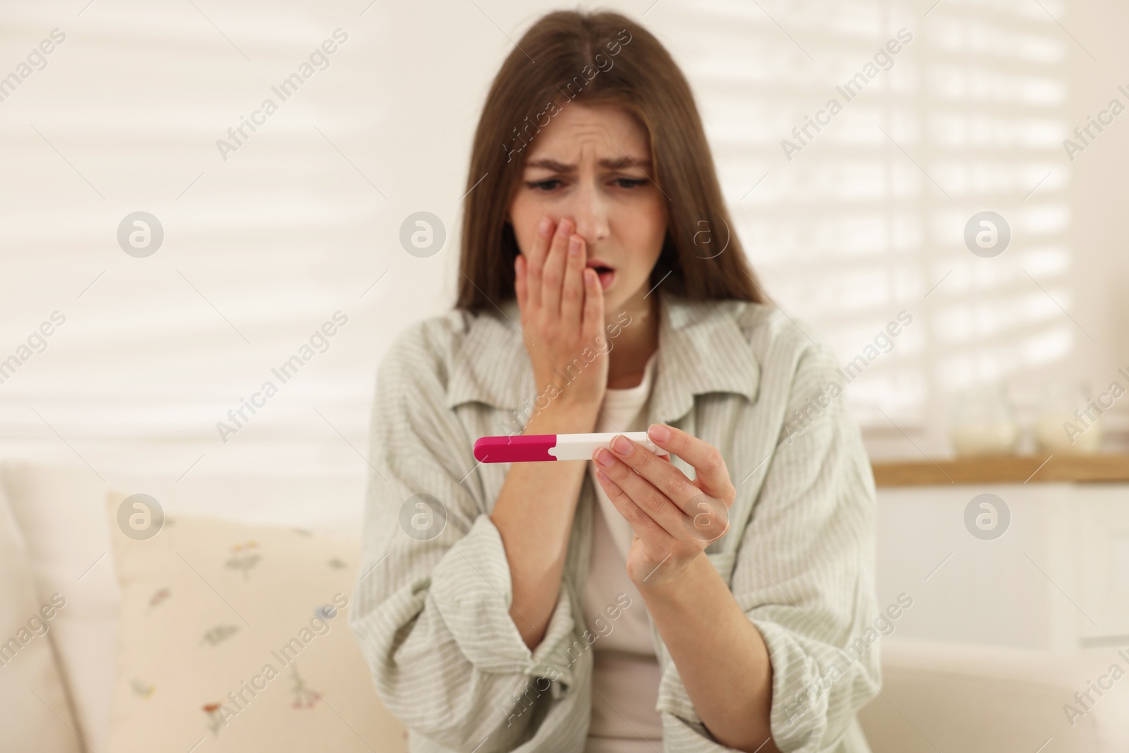 Photo of Upset woman with negative pregnancy test on sofa at home, selective focus