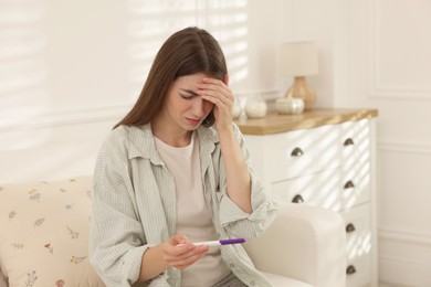 Photo of Upset woman with negative pregnancy test on sofa at home