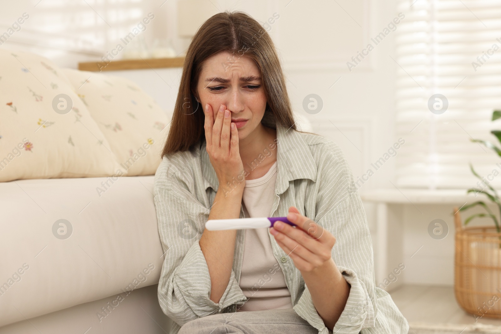 Photo of Upset woman with negative pregnancy test at home