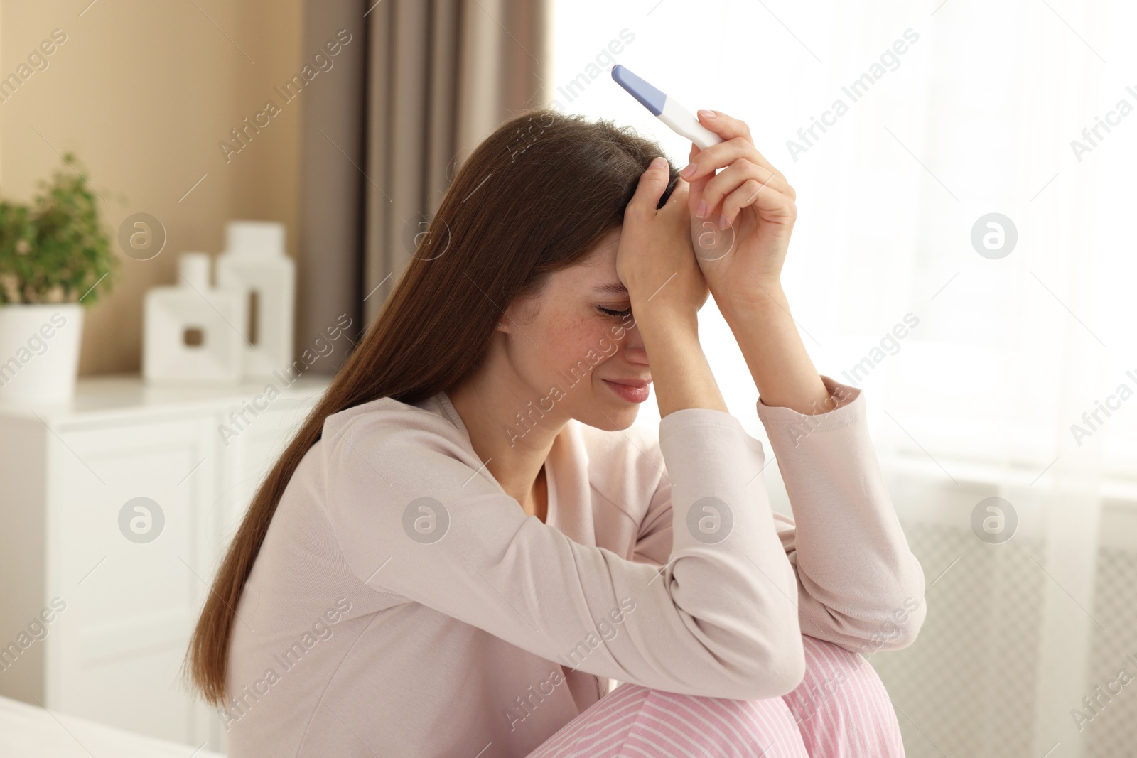 Photo of Upset woman with negative pregnancy test at home