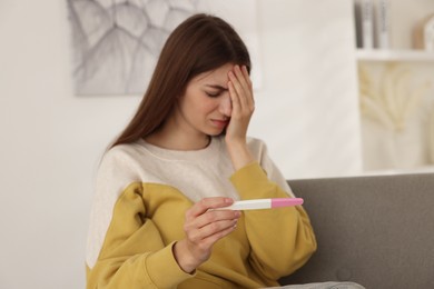 Photo of Upset woman with negative pregnancy test on sofa at home