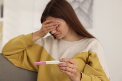 Photo of Upset woman with negative pregnancy test on sofa at home, selective focus