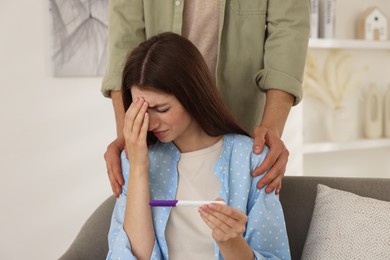 Photo of Upset woman with negative pregnancy test indoors. Man supporting his wife at home