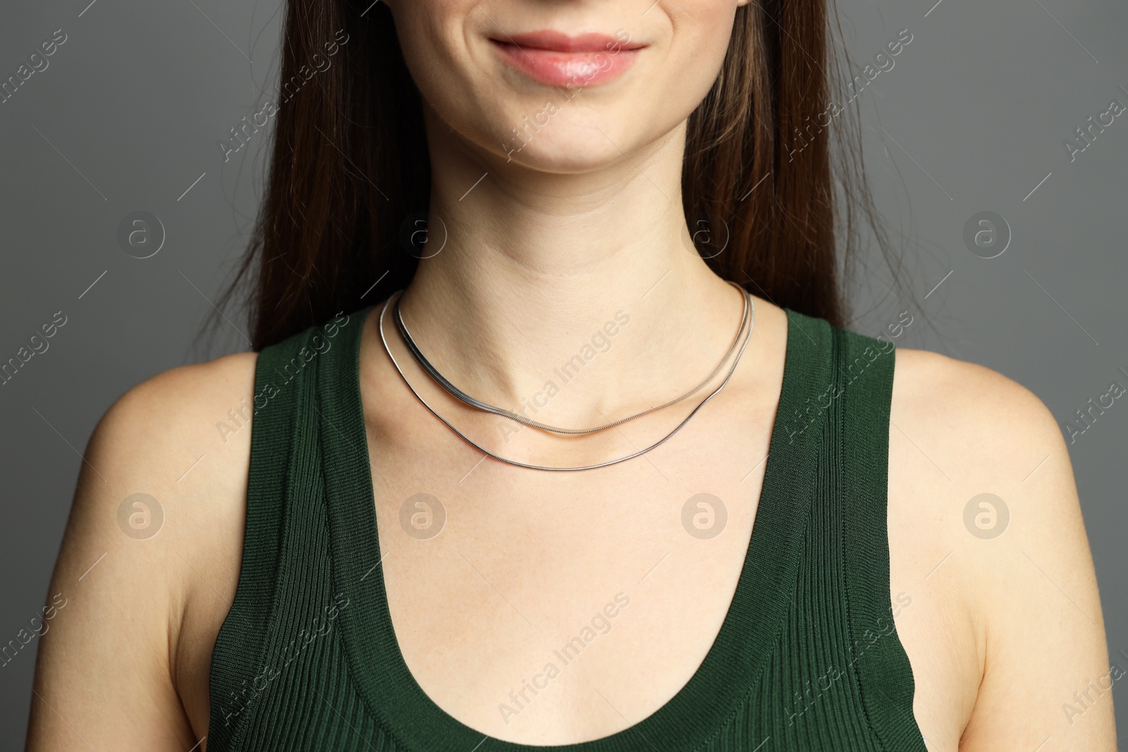 Photo of Woman wearing layered silver necklace on grey background, closeup